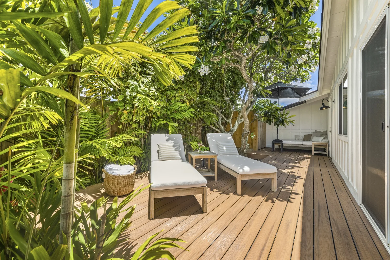 A wooden deck patio has lounge seating surrounded by dense tropical greenery.