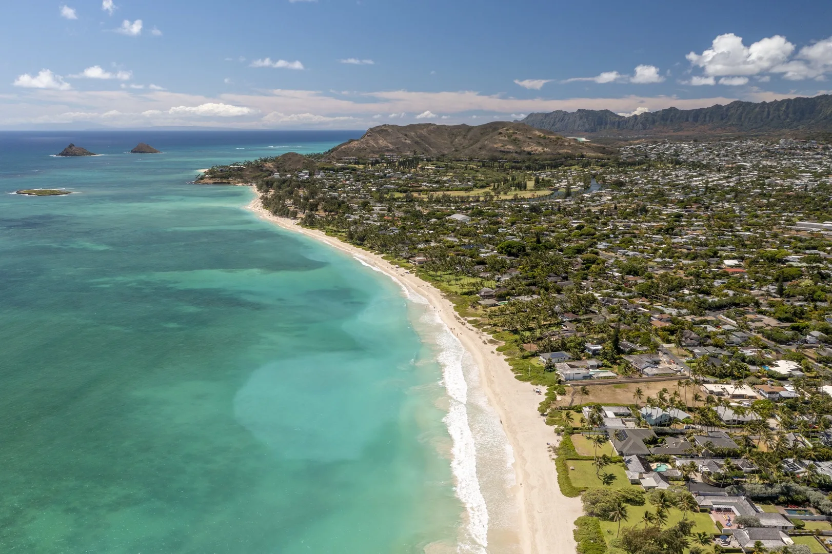 Aerial view of a curving coastline with turquoise water, sandy beach, and nearby homes.