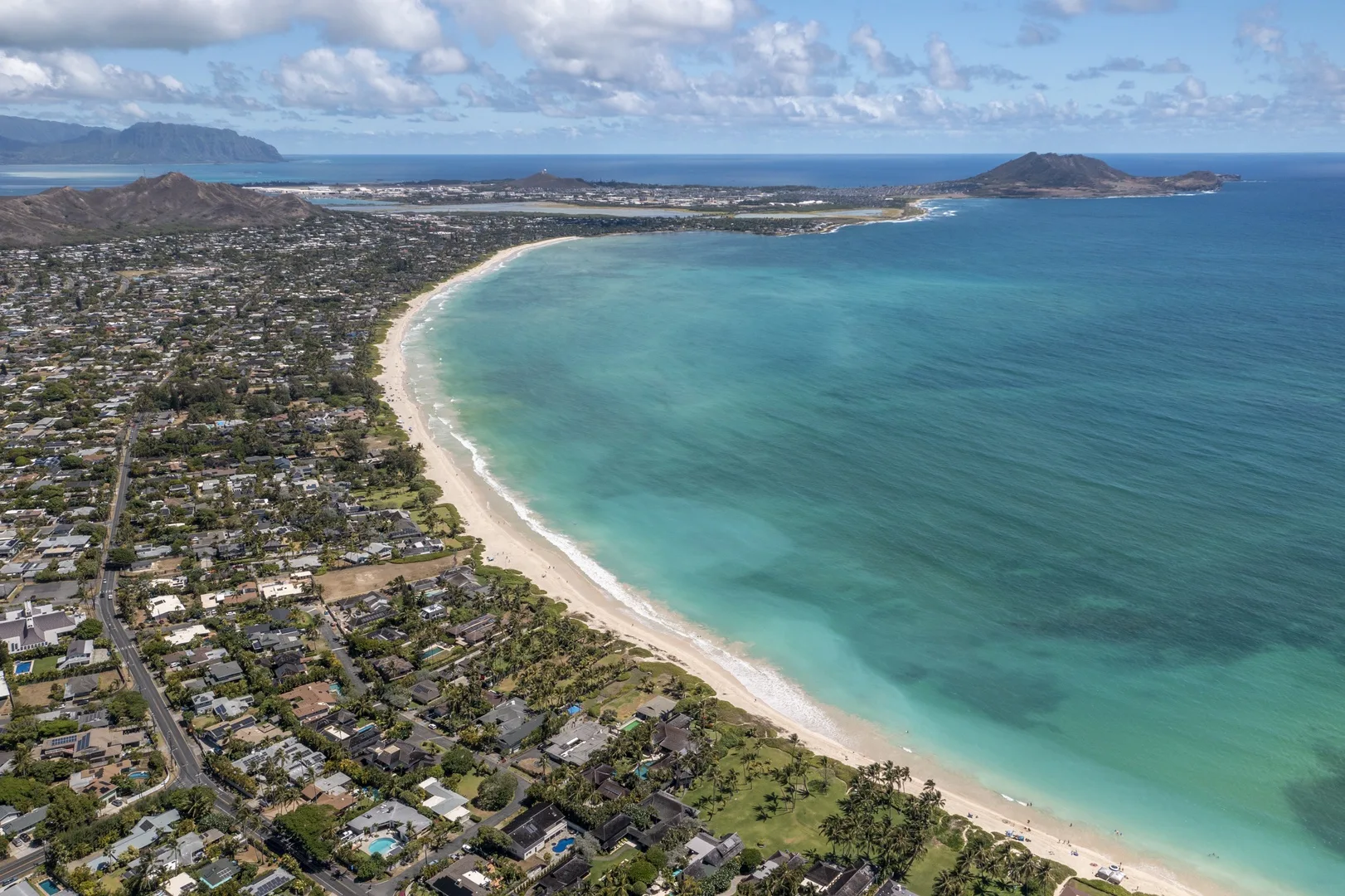 Aerial view of a long sandy beach curving around a coastal neighborhood.