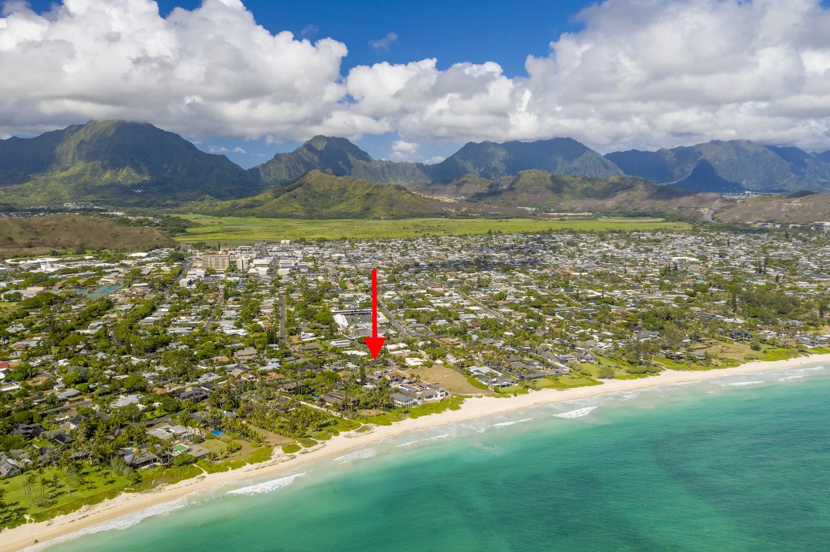 Aerial view of a coastal neighborhood beside a sandy beach, with mountains in the distance.