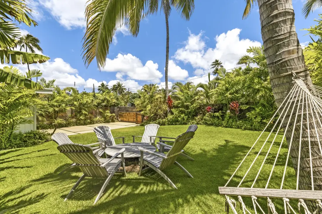 A tropical garden seating area with lawn chairs beneath palm trees.