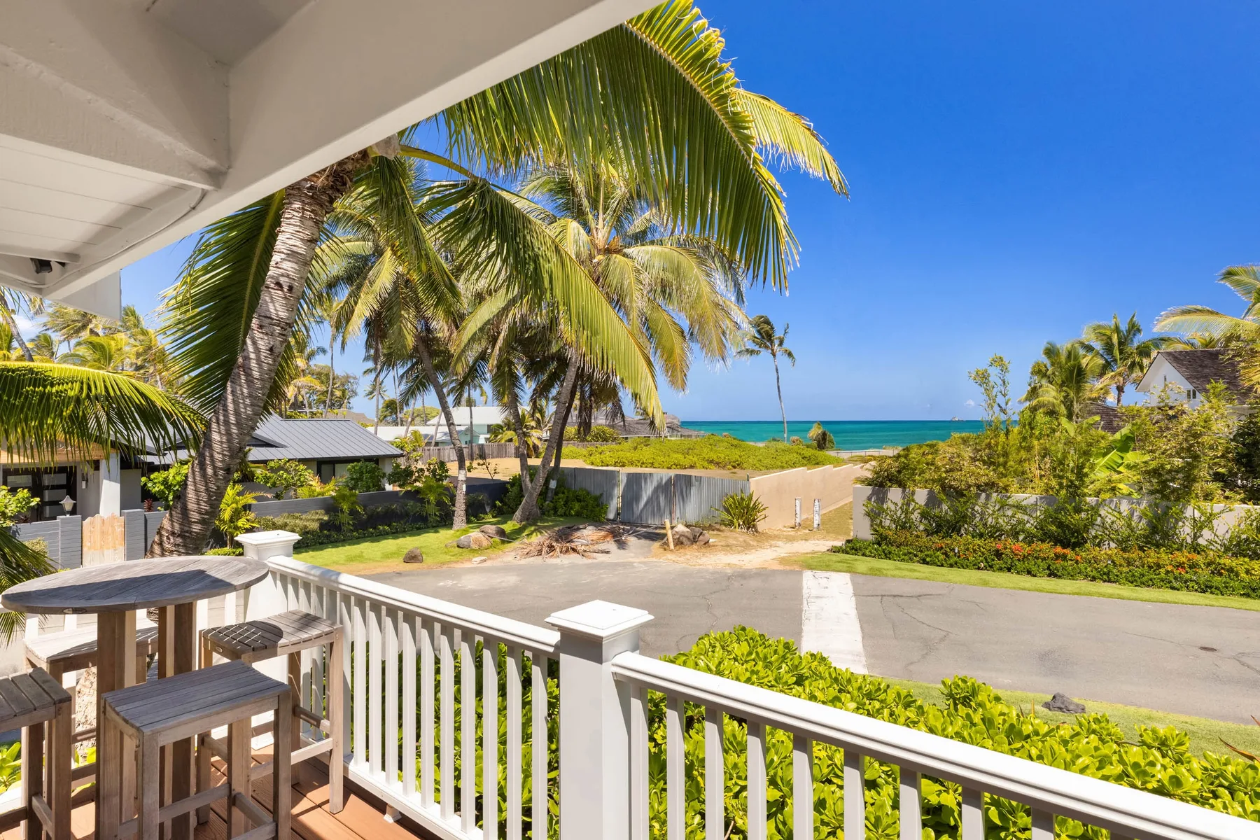 A covered balcony overlooks a tropical shoreline with palm trees and blue water.