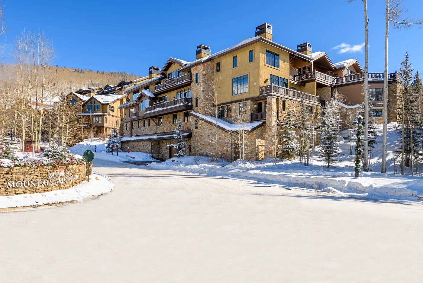 A large lodge stands beside a snow-covered road among evergreen trees.