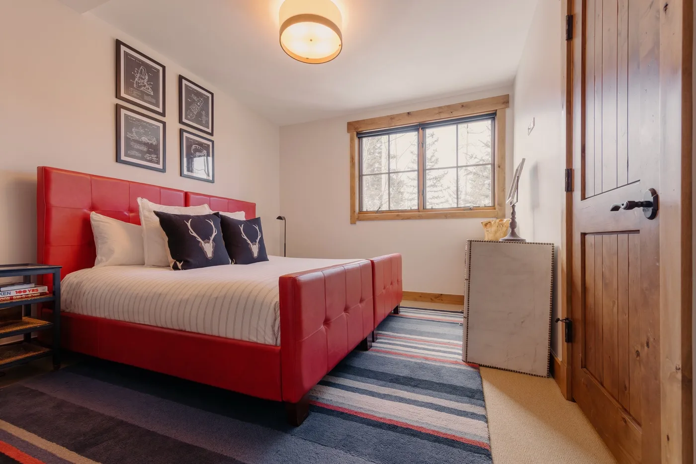 A bedroom with a red upholstered bed, striped rug, and a window.