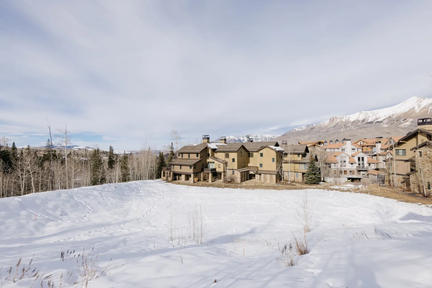 Snow-covered ground stretches toward a cluster of buildings beneath a mountain ridge.