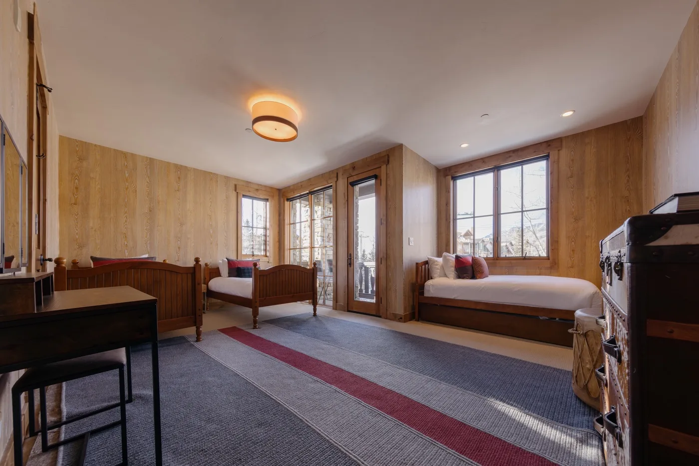 Bedroom with two beds, large windows, and wood-paneled walls.