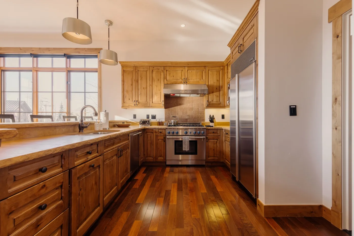A warm-toned kitchen with wooden cabinets, a central stove, and a stainless steel refrigerator.