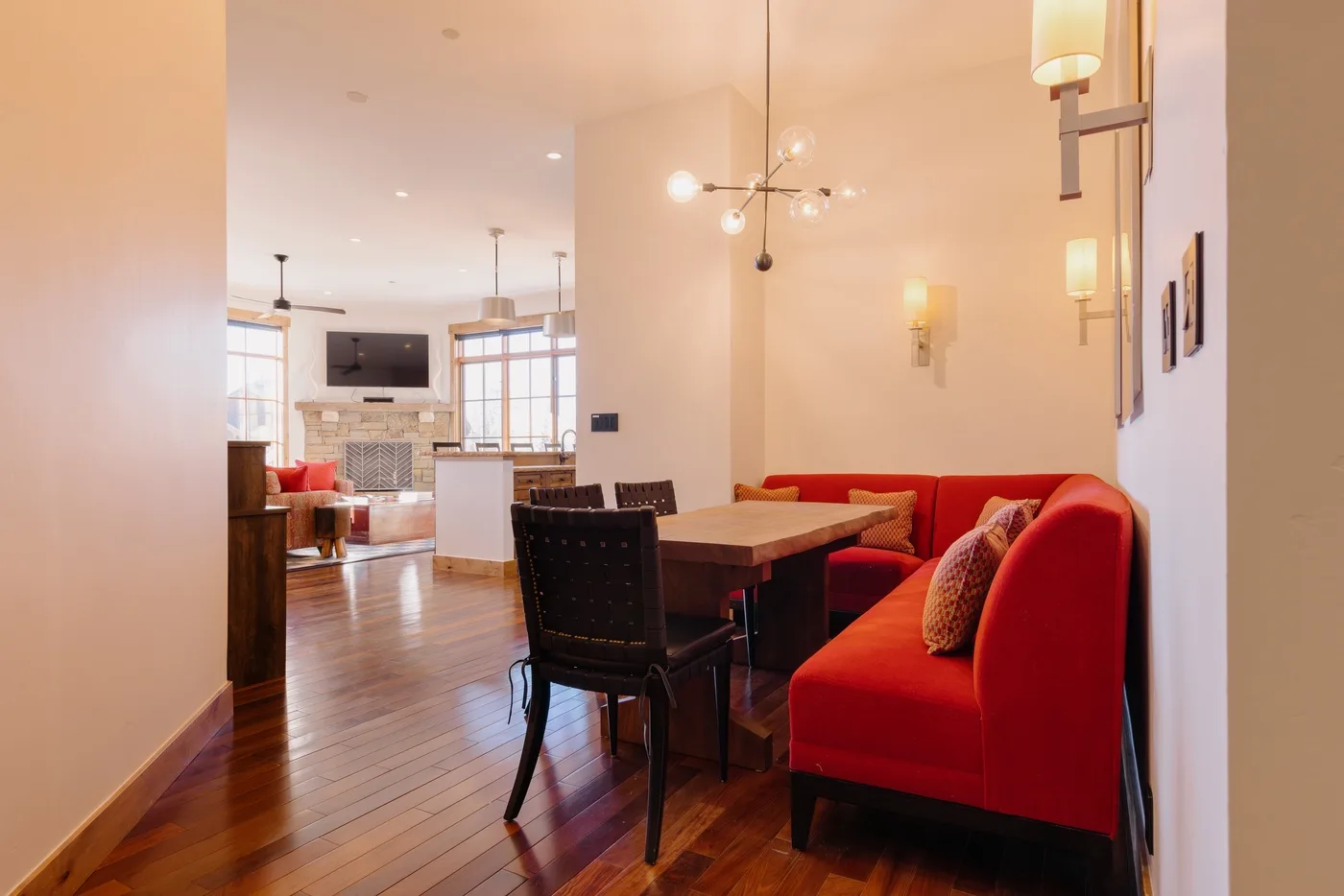 A dining area with a wooden table and red seating opens onto a living room.