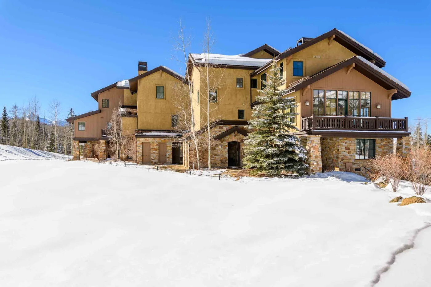 A large lodge-style building stands beside a snow-covered open area under a clear blue sky.