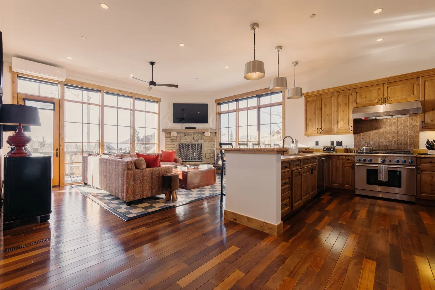 A bright open-plan living room and kitchen with large windows and wood cabinetry.