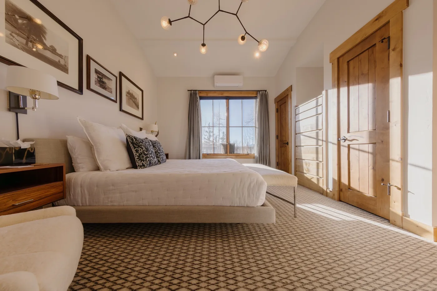 A bright bedroom with a bed, patterned carpet, and wooden doors.
