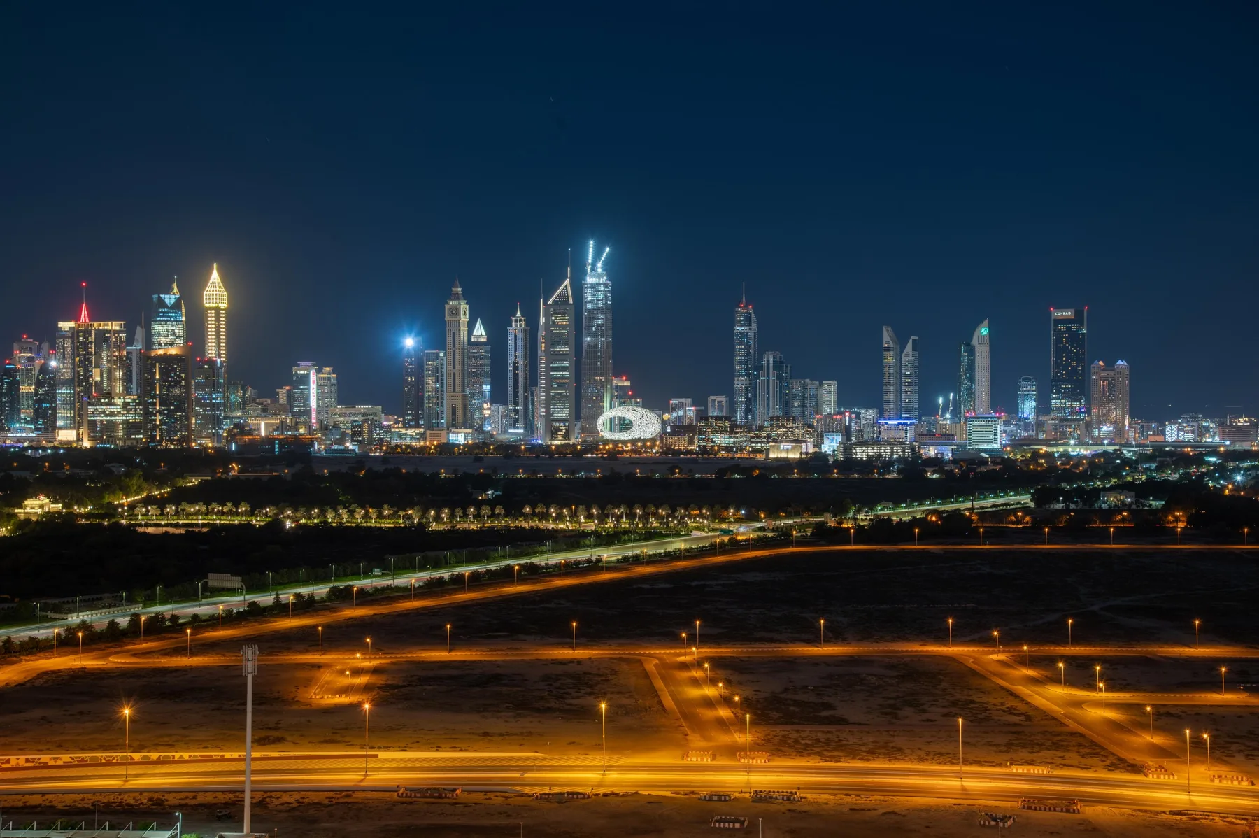Nighttime city skyline with illuminated skyscrapers and roads in the foreground.