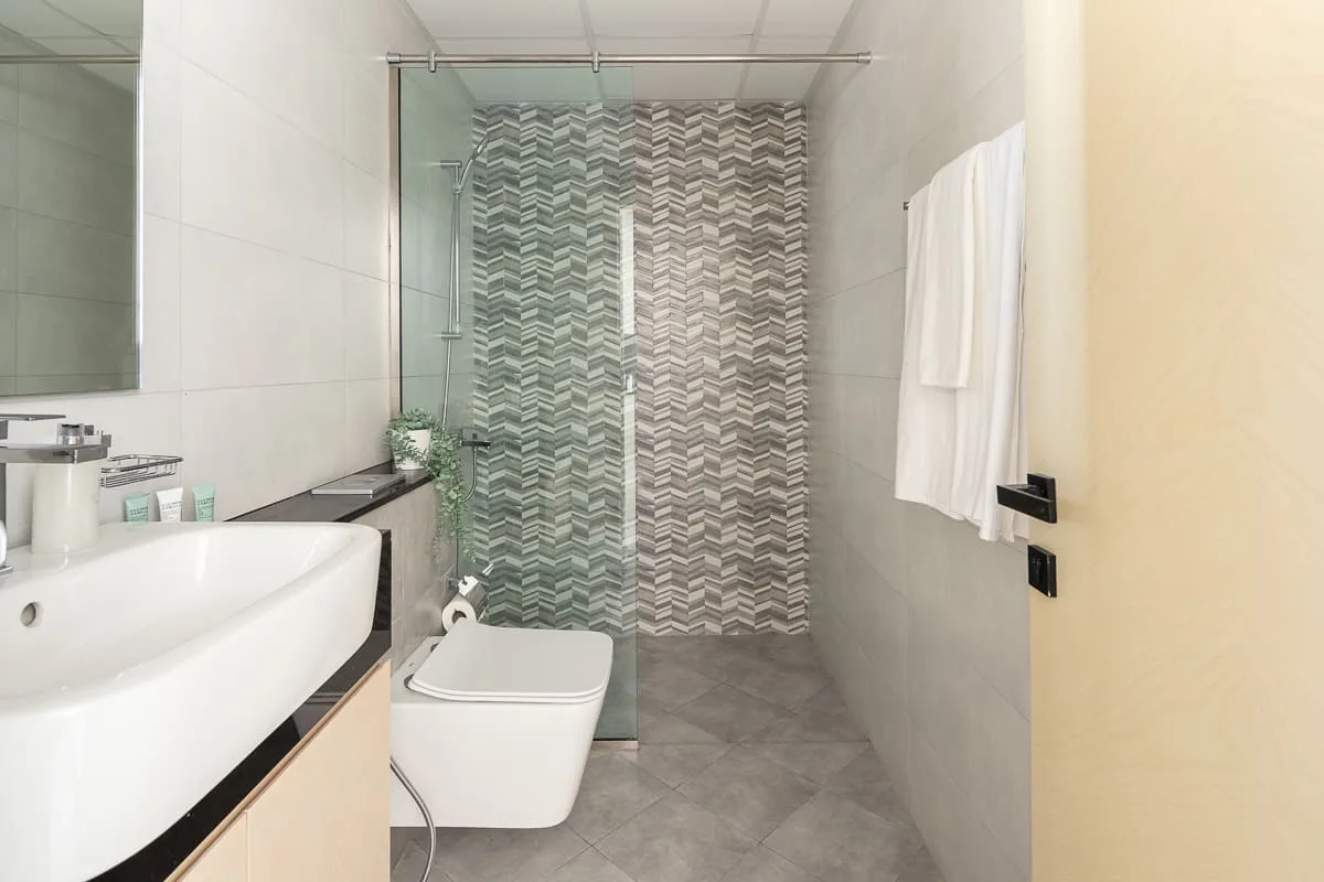 A modern bathroom with a sink, toilet, and patterned shower wall.
