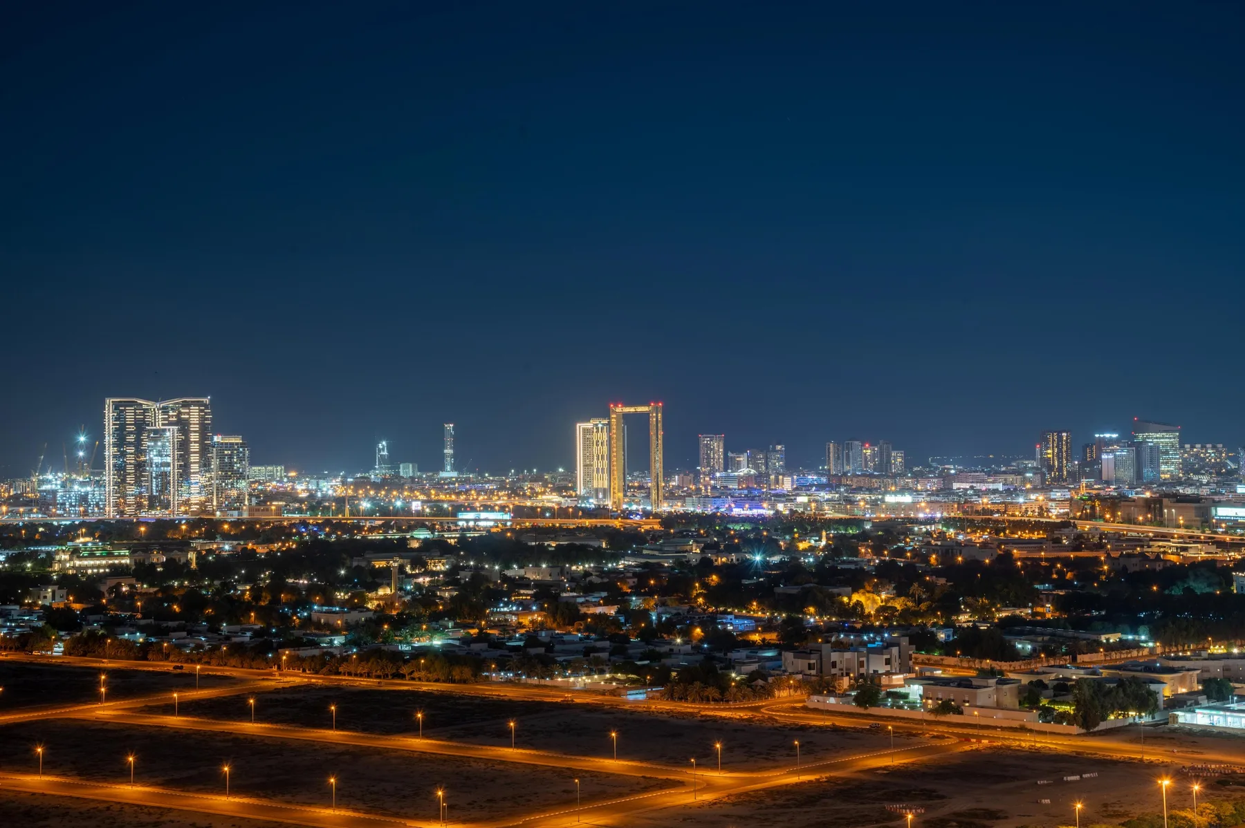 A city skyline at night glows above illuminated roads and neighborhoods.