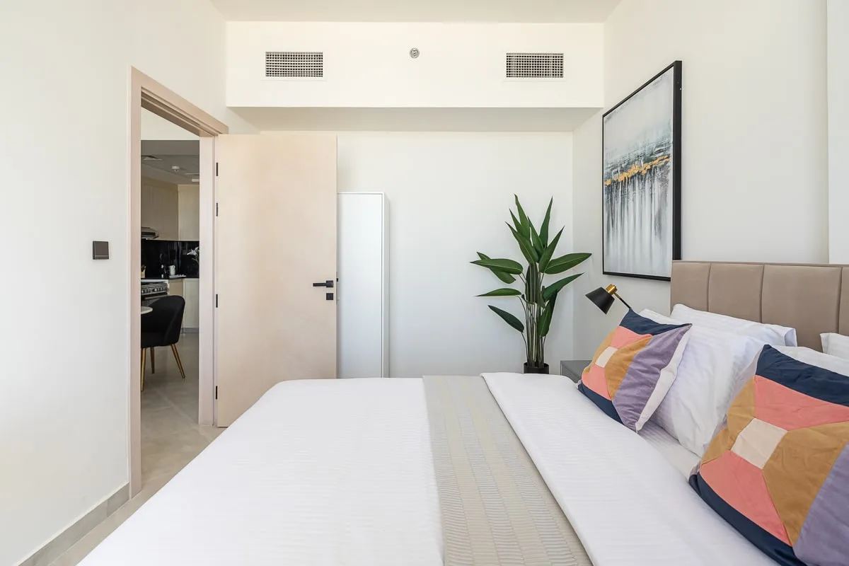 A bright bedroom with a neatly made bed and colorful pillows.