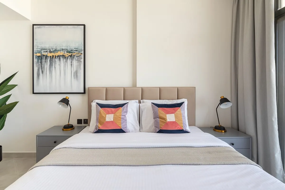 A bedroom with a neatly made bed, colorful pillows, and bedside lamps.