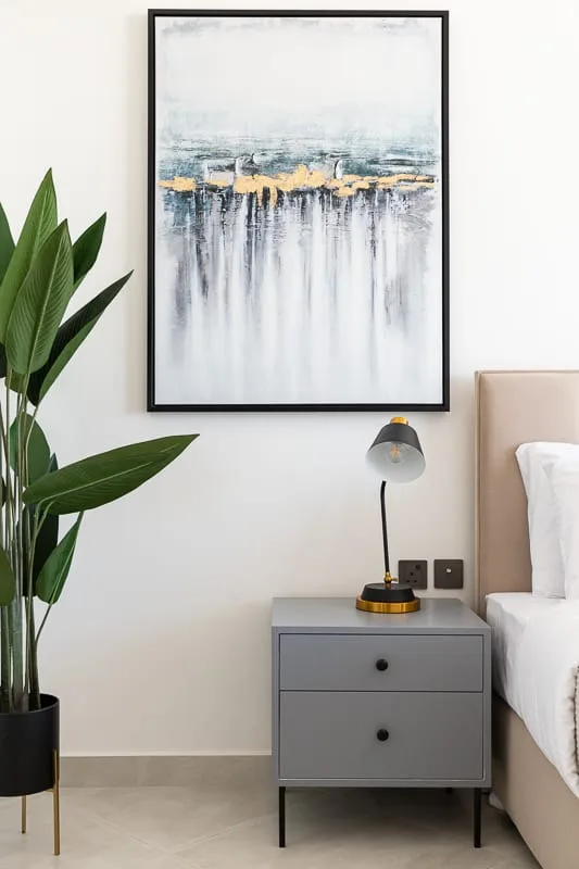 A bedroom bedside area with a gray nightstand, lamp, and abstract wall art.