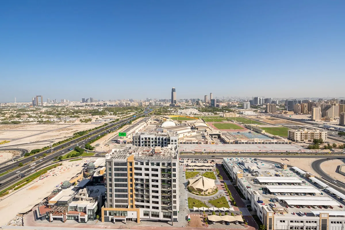 A city skyline and surrounding buildings are viewed from above under a clear blue sky.