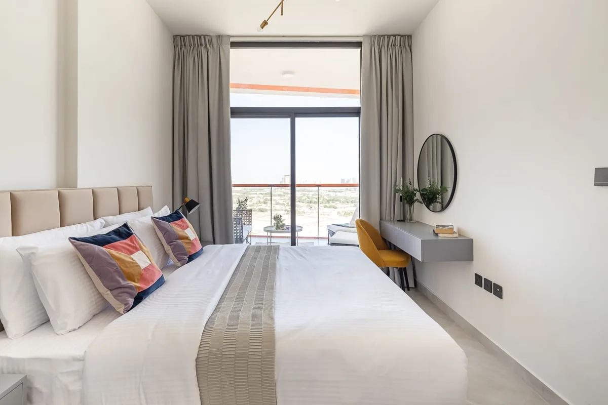 A bright bedroom with a large bed facing a window and glass doors.