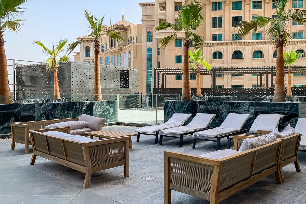 An outdoor seating area with cushioned lounge chairs and palm trees.