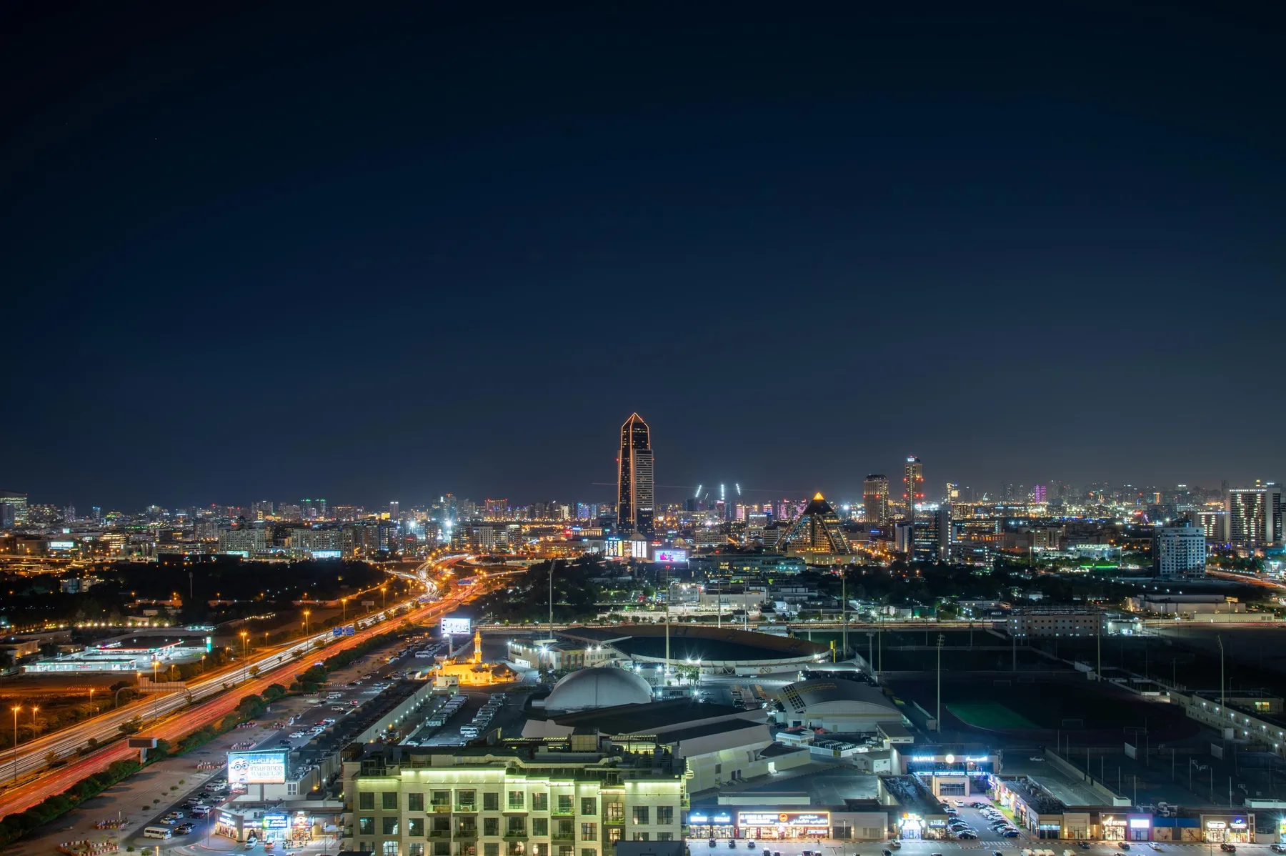 A nighttime city skyline glows above illuminated roads and buildings.