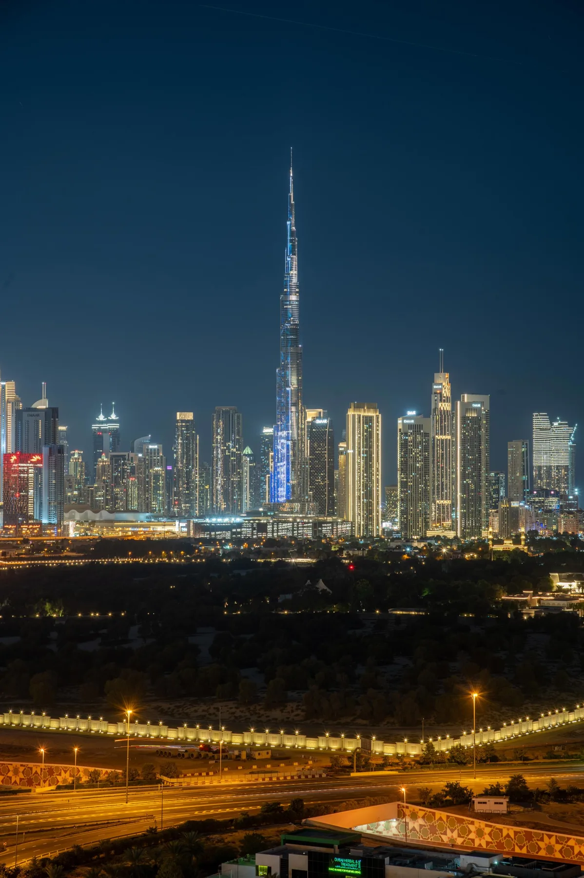 A nighttime city skyline features a very tall illuminated tower above the surrounding buildings.