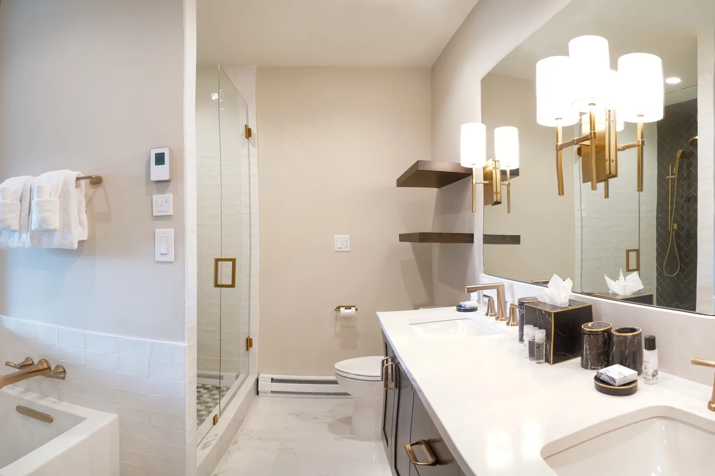 A bright bathroom with a glass shower, toilet, and long vanity beneath a large mirror.