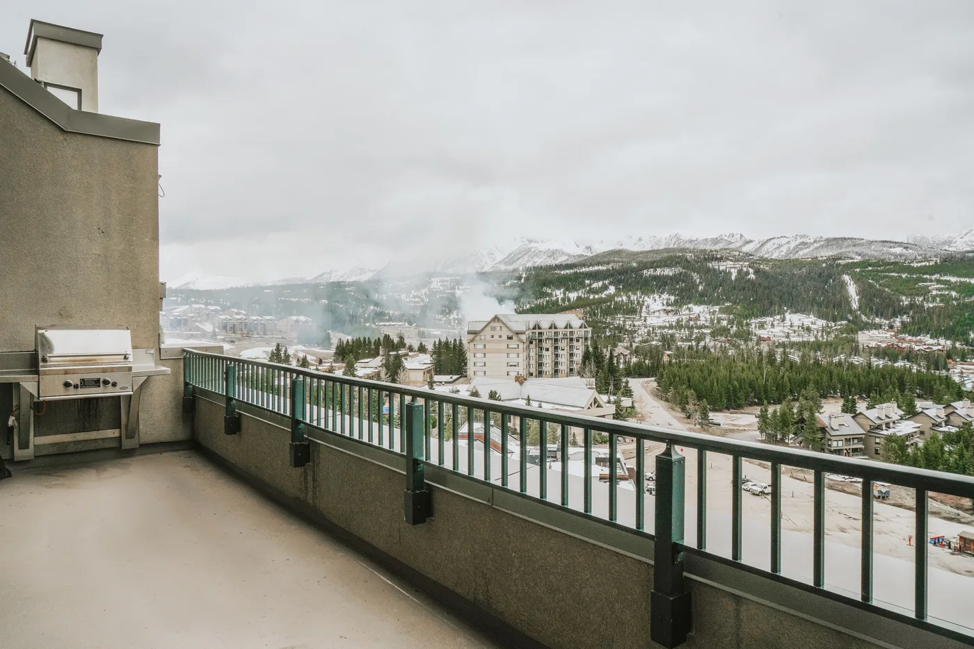 A balcony overlooks a snow-covered mountain town beneath a cloudy sky.