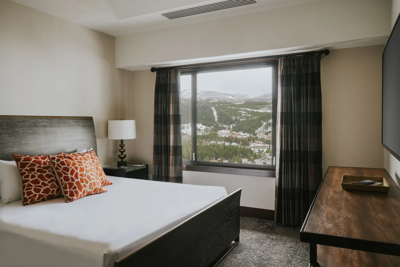 A bedroom with a bed, bedside lamp, and a window overlooking a snowy landscape.