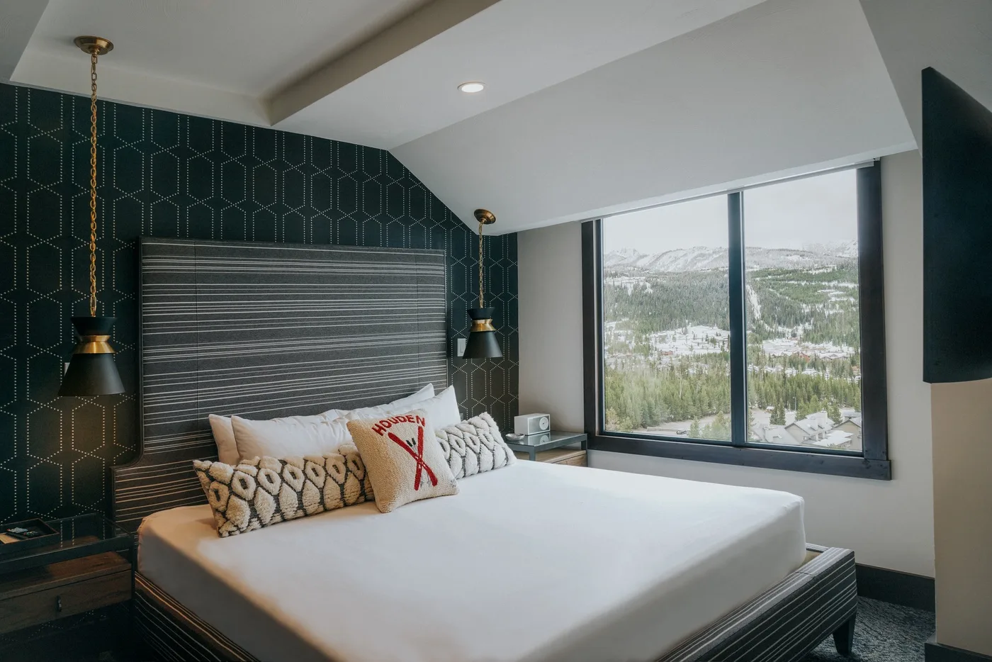 A bedroom with a neatly made bed beside large windows overlooking a snowy landscape.