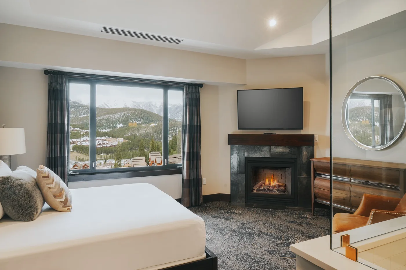 A bedroom with a bed, a fireplace, and a large window overlooking a snowy landscape.