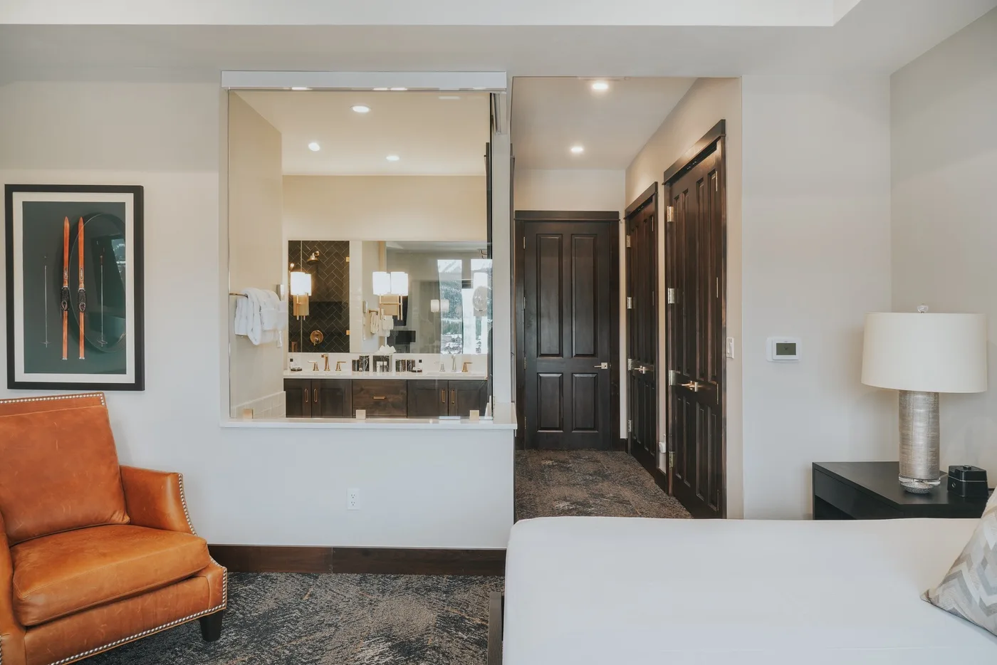A bedroom with a bed and orange seating beside an open bathroom vanity.