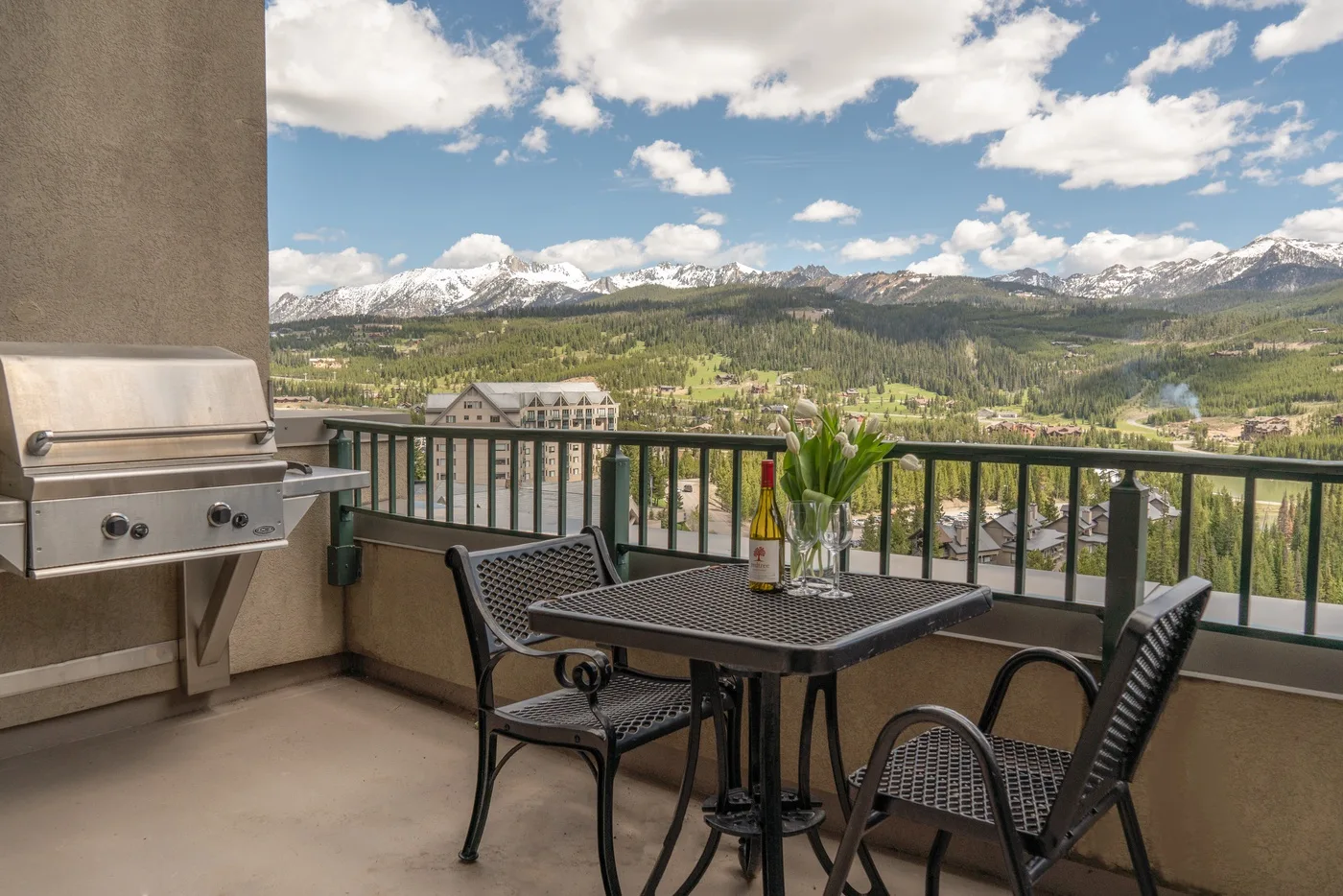 A balcony dining area overlooks a green valley and snow-capped mountains.