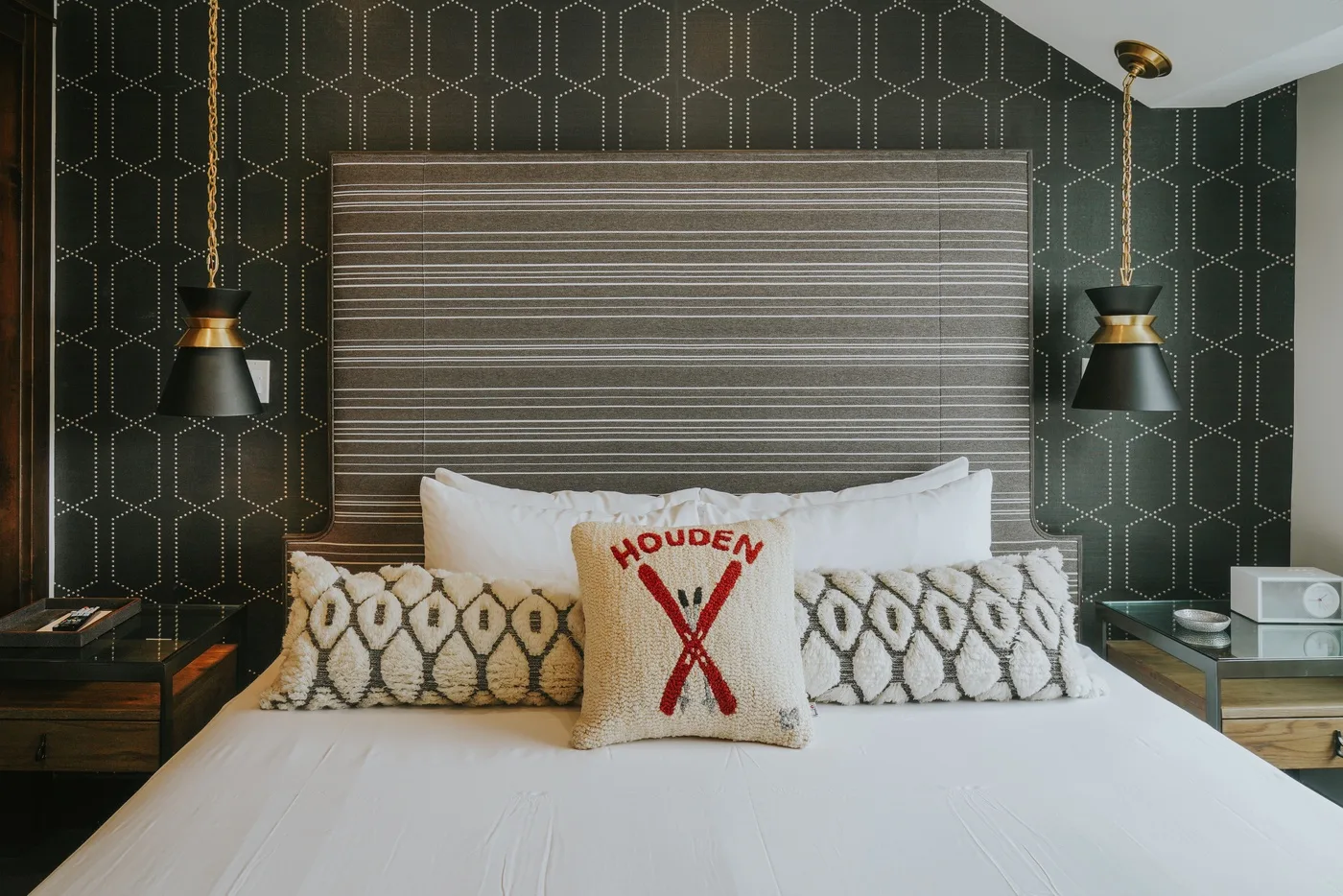 A bedroom with a neatly made bed and patterned dark wallpaper.