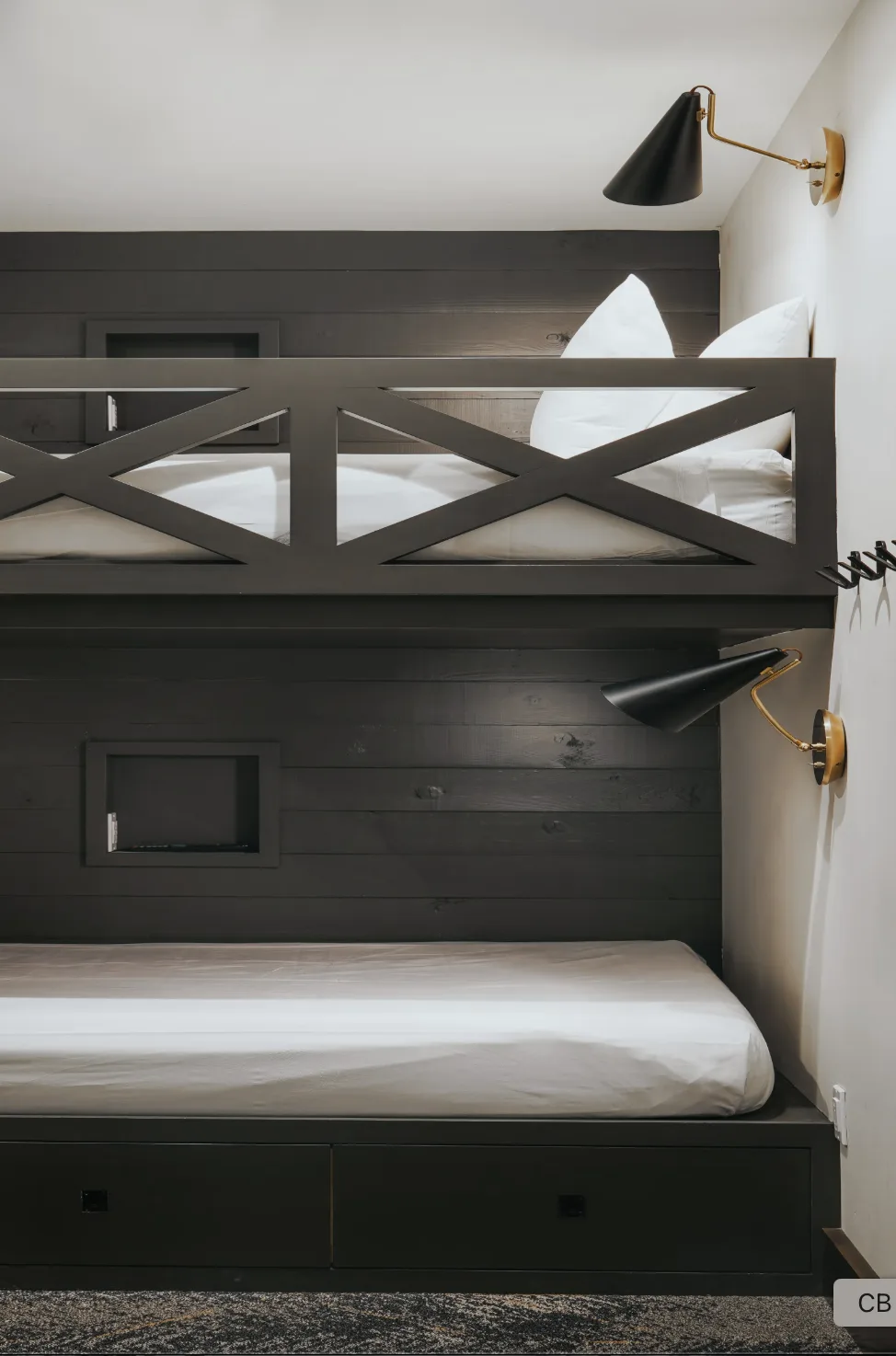 A dark built-in bunk bed with white bedding and wall-mounted lights.