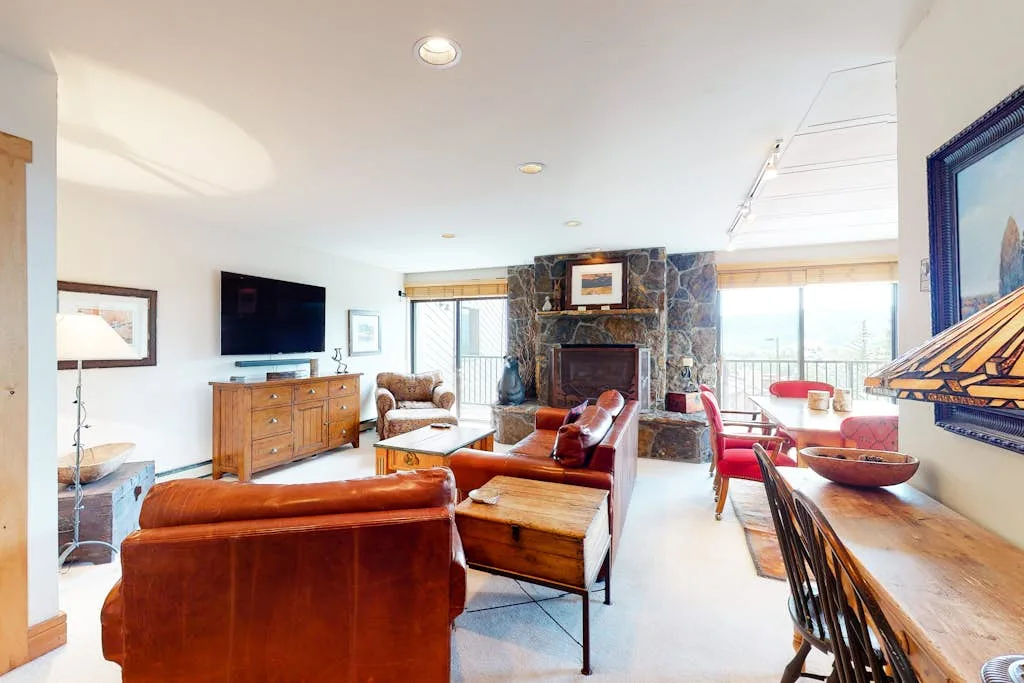 A bright living room with leather seating, a stone fireplace, and a dining table.