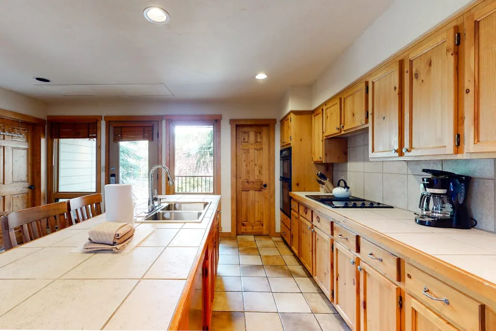 A bright kitchen with wooden cabinets, tiled counters, and a central island.