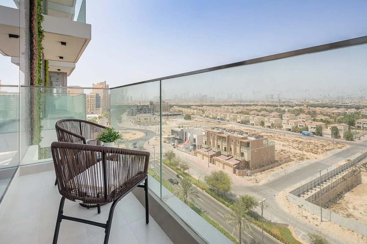 A balcony with dark seating overlooks a neighborhood of low-rise buildings.