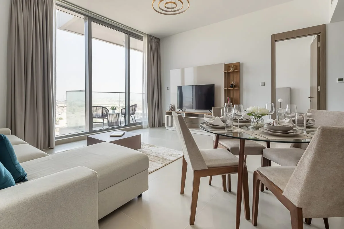 A bright living and dining area with floor-to-ceiling windows and a glass dining table.