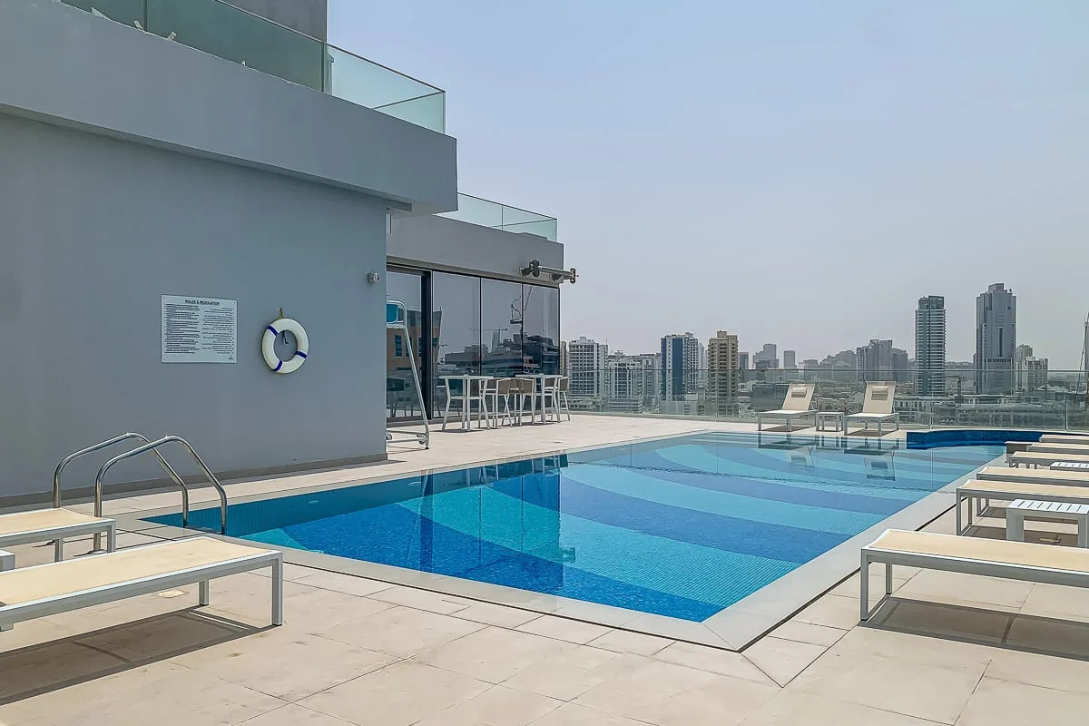 A rooftop swimming pool is surrounded by lounge seating and overlooks a city skyline.