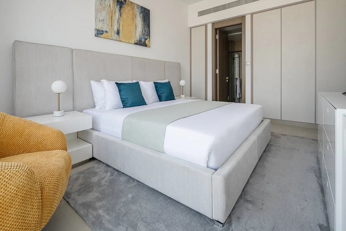 A bright bedroom with a neatly made bed and teal accent pillows.