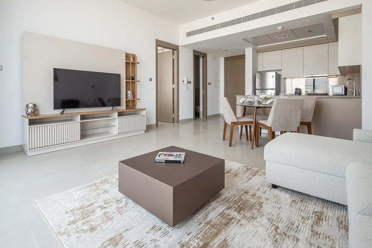 A bright living room opens into a dining area and kitchen, with a television and seating.