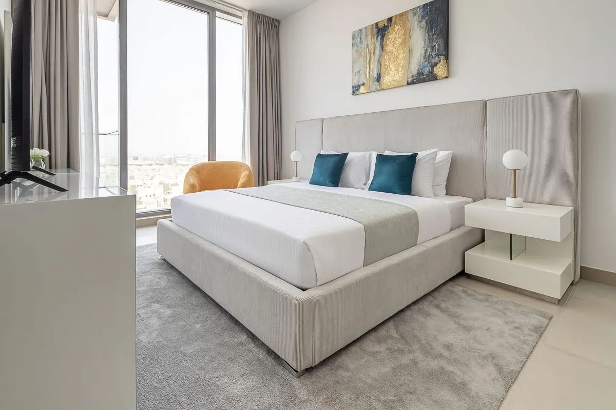 A bright bedroom with a neatly made bed beside a large window.