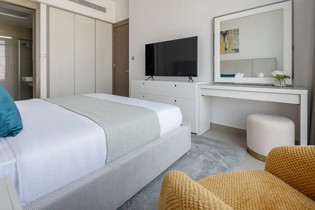 A bright bedroom with a bed, television, and dressing table.