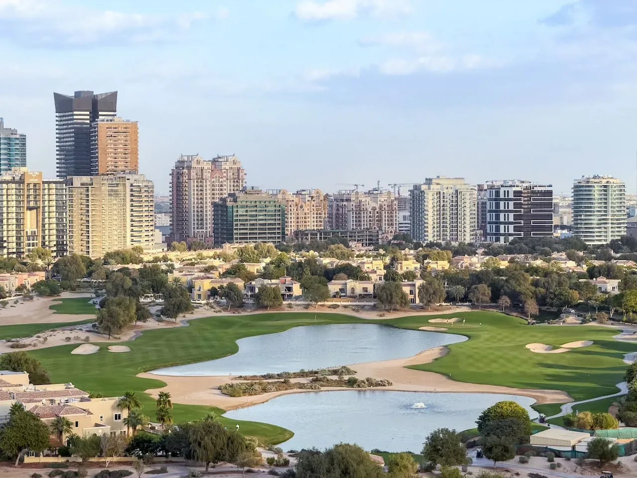 A golf course with water features and green fairways sits below a city skyline.