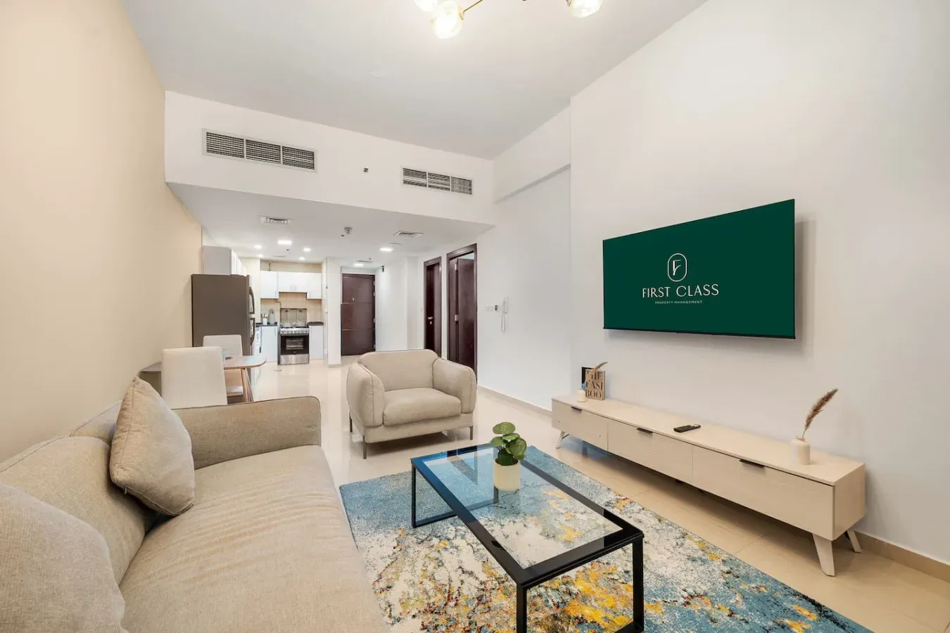 A bright living room with seating, a glass coffee table, and a wall-mounted television.