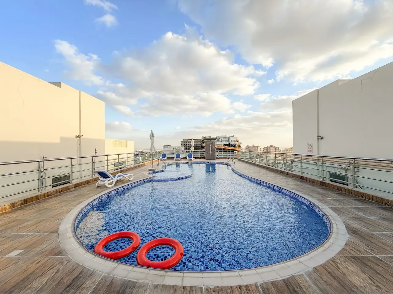 A rooftop swimming pool with blue mosaic tiles and two red flotation rings.