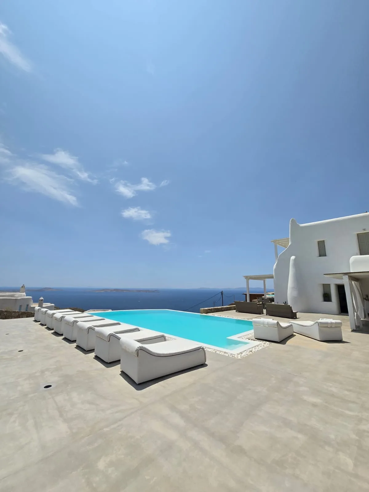 Una piscina al aire libre junto a un edificio blanco, con asientos orientados hacia el mar.