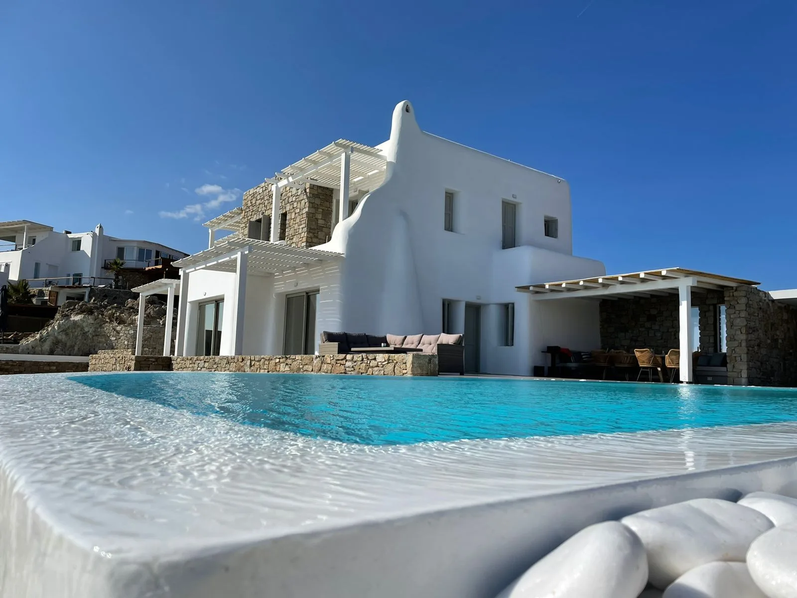 Una villa blanca está junto a una piscina turquesa bajo un cielo azul despejado.