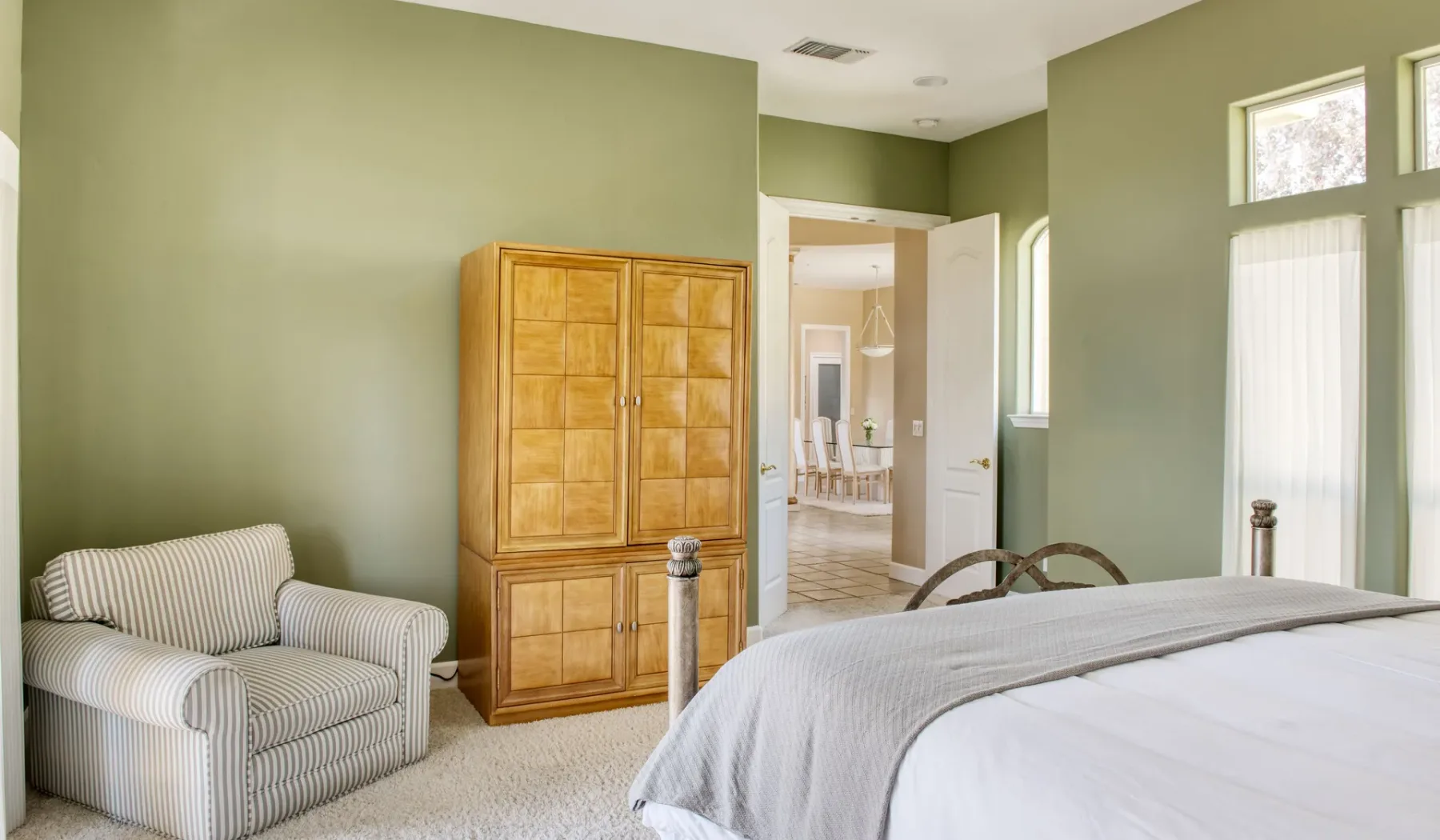 Dormitorio con un armario de madera, un sillón a rayas y una cama.